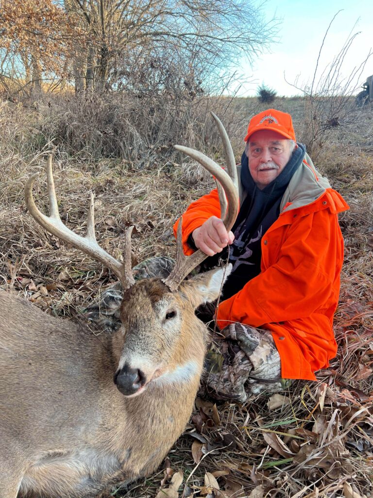 Man posing with deer trophy after successful hunt in trees.