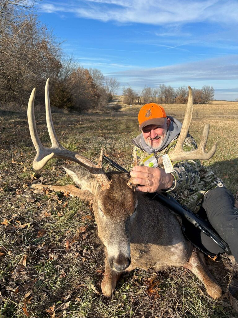 Man posing with deer trophy after successful hunt in field by forest.