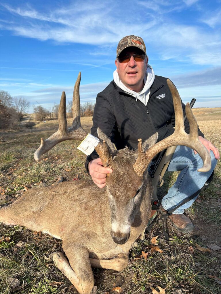 Man posing with deer, smiling with hat.