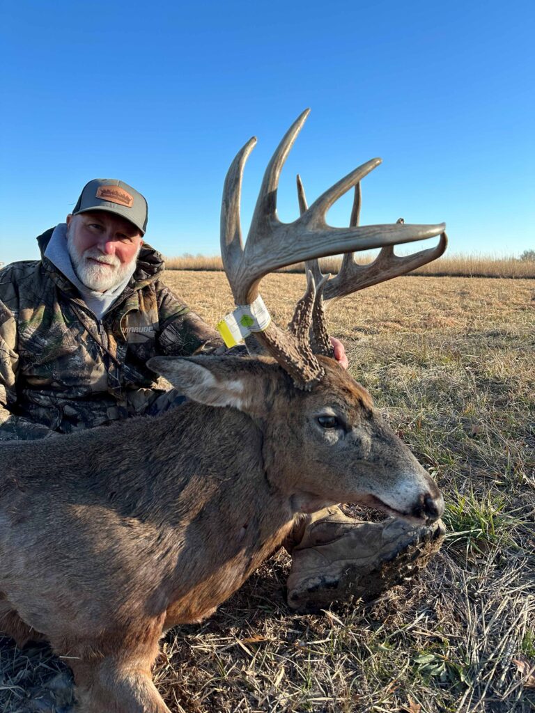 Man posing with deer, smiling with hat.