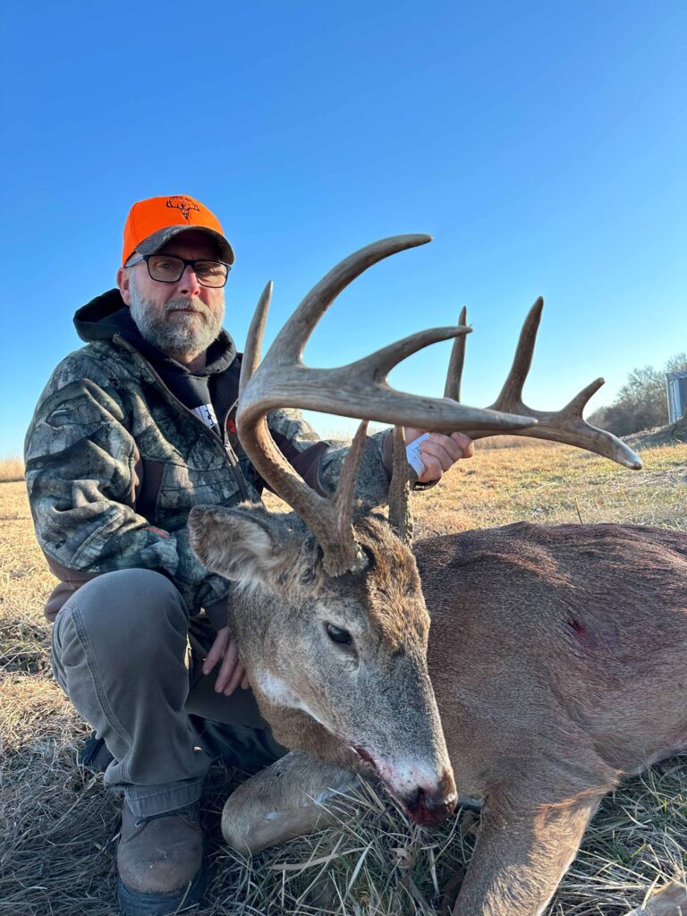 Man posing with deer, smiling with hat.