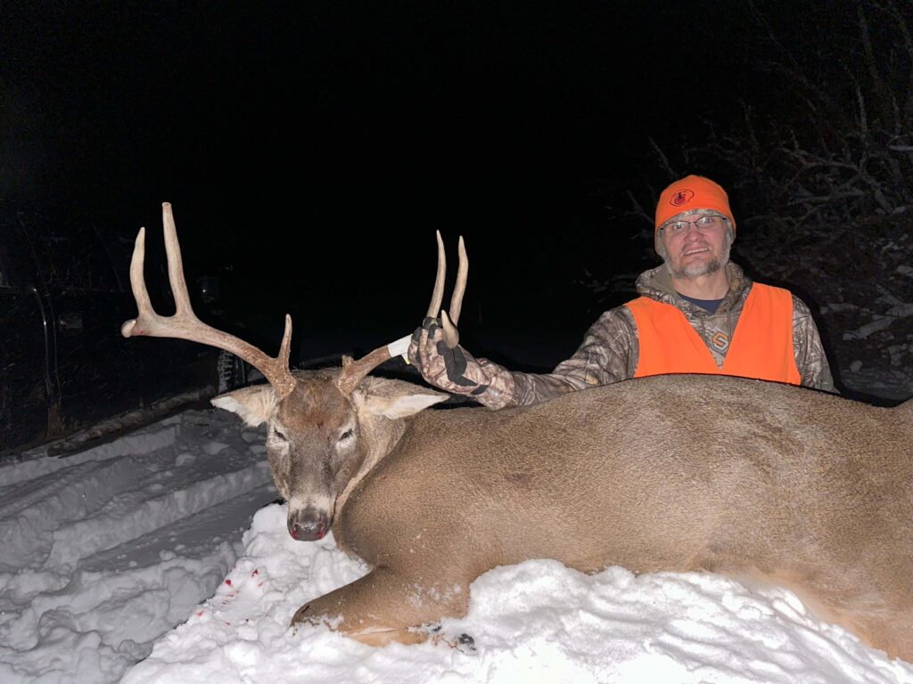 Man posing with deer. Smiling in the snow.